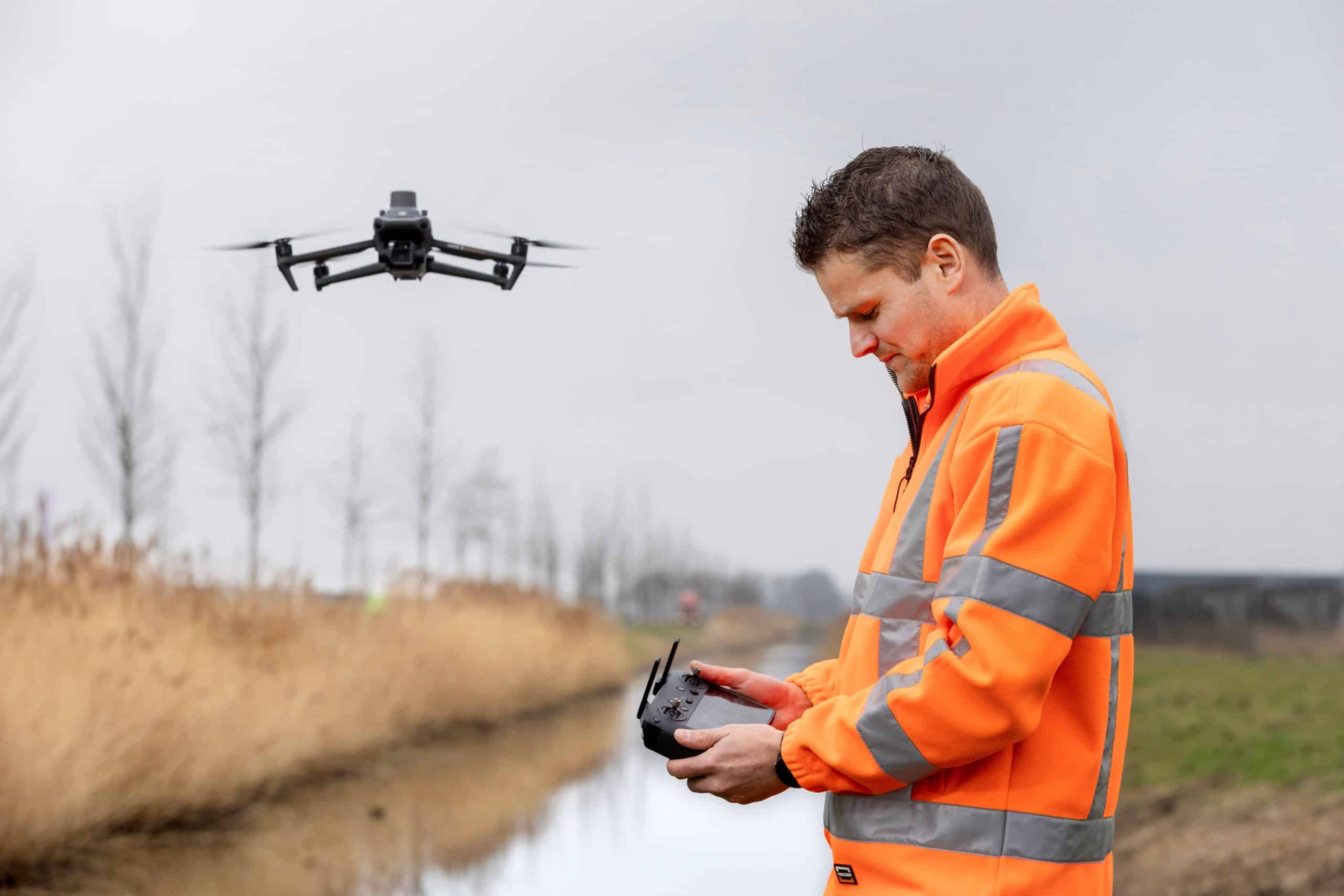 Man in werkkleding kijkt naar afstandsbediening en laat drone vliegen in het natuurgebied waar hij staat.