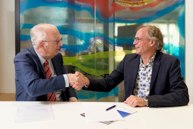 Twee mannen schudden elkaar de hand na het ondertekenen van een document.